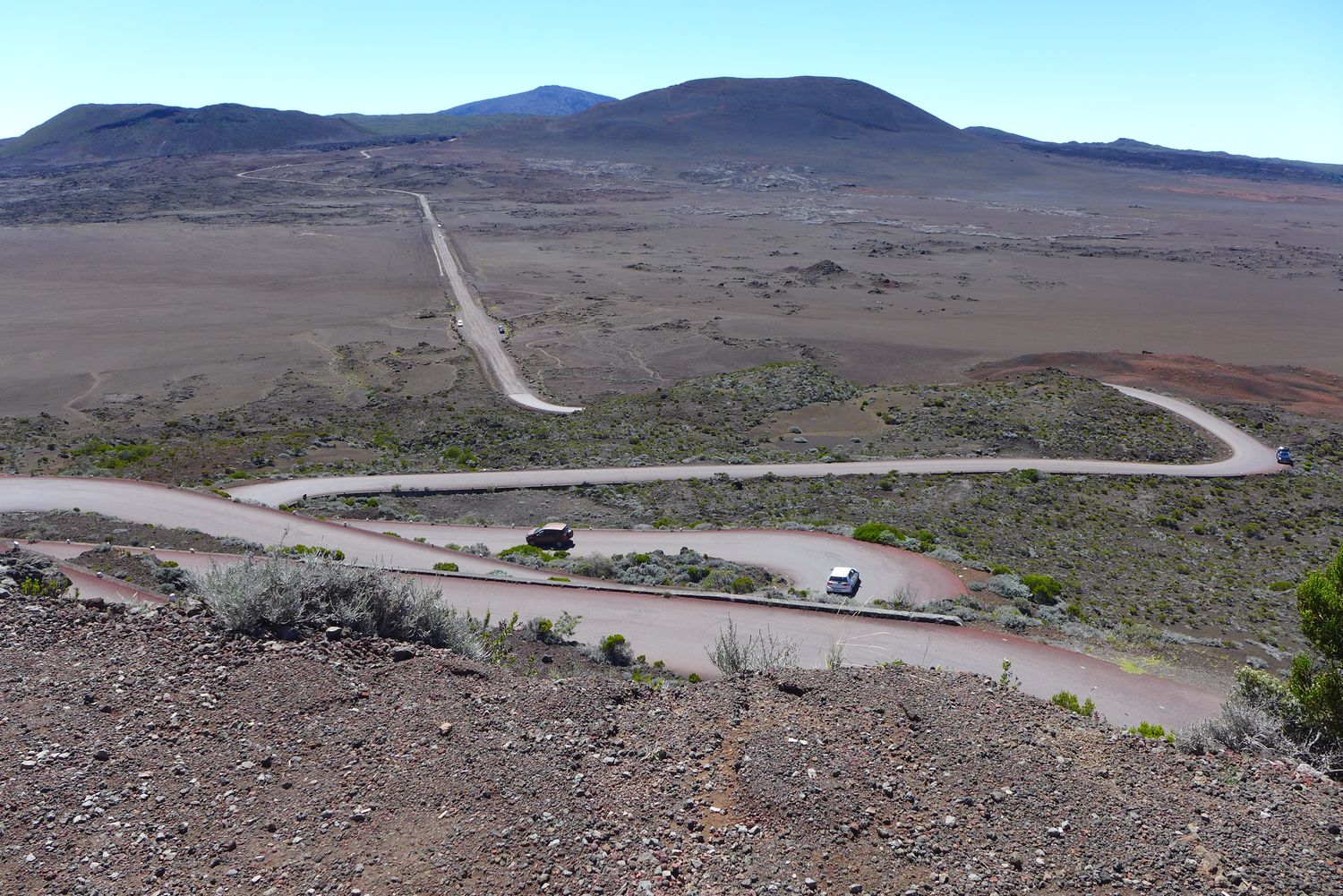 La route en contrebas, caillouteuse, nous mène jusqu’au Pas de Bellecombe, d’où l’on peut observer le Piton de la Fournaise. C’est aussi le départ de la randonnée qui mène jusqu’au sommet du cratère. Le chemin de randonnée est fermé lorsque le Piton entre en éruption.