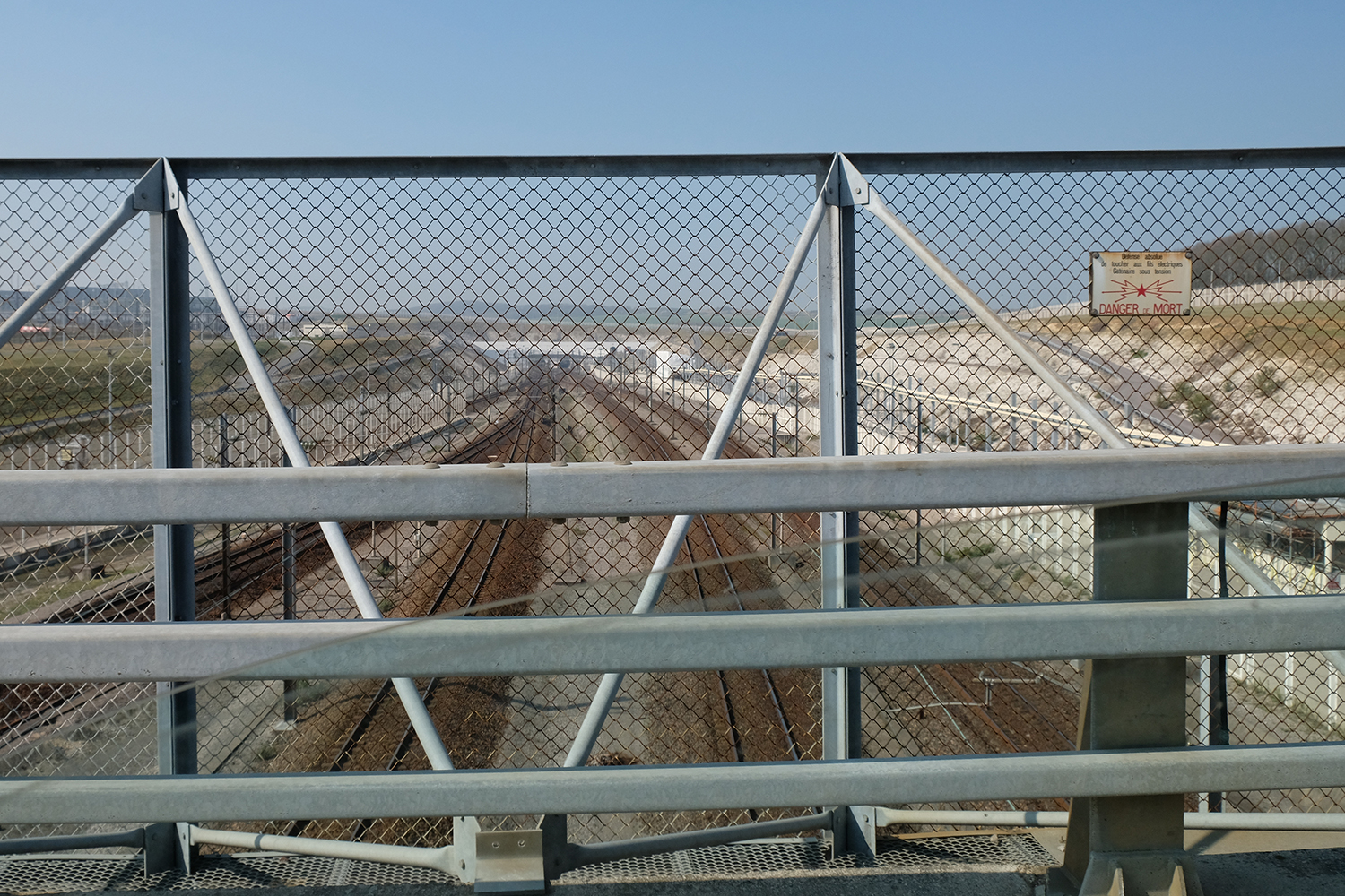A quoi ressemble une frontière ? Quelques mètres plus loin, un pont nous amène au dessus des rails du tunnel sous la manche. En contre bas des voitures de police et des douanes surveillent le passage.